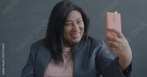 Slow motion portrait of pretty young lady taking selfie posing for smartphone camera on black background. Photography and modern technology concept.