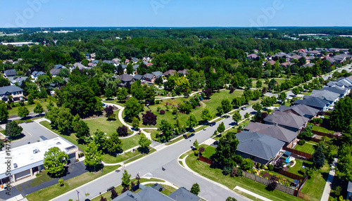 Aerial view of a suburban neighborhood showcasing houses, green parks, and winding roads under clear skies
