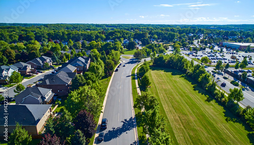 Aerial view of a suburban neighborhood with tree-lined streets and a shopping area in the background