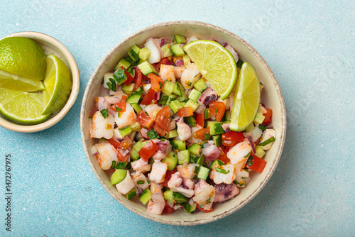 Fresh and vibrant peruvian seafood ceviche with shrimps, octopus, tomatoes, cucumber and parsley, served with lime in a bowl on a light blue background from above, dish of Peru photo