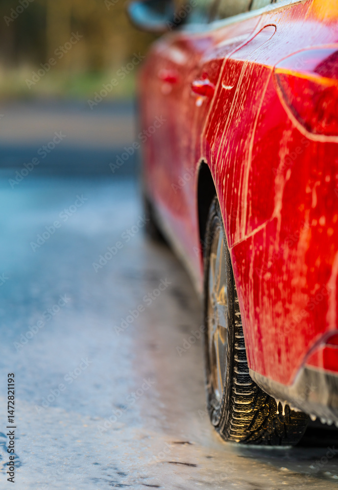 Red vehicle covered in soap during wash.