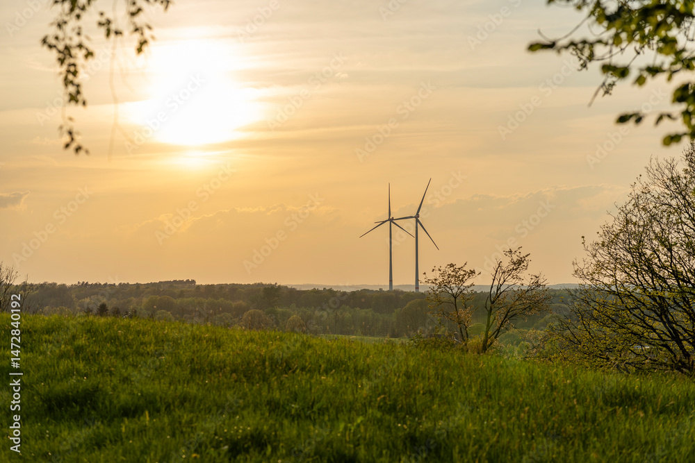 Obraz premium Two wind turbines standing next to each other in an orange-red sunset in the German countryside. Green energy concept