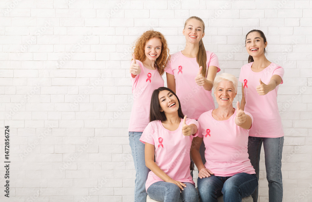 Obraz premium Diverse Female Volunteers In Pink Breast Cancer T-Shirts With Ribbons Gesturing Thumbs-Up Posing Over White Brick Wall. Copy Space