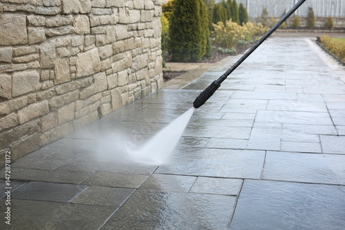 Pressure washer cleaning a stone patio near a house wall and garden.