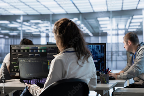 IT staff member programming in AI server farm housing advanced equipment used for machine learning training. Woman running code on laptop to upgrade artificial intelligence rigs