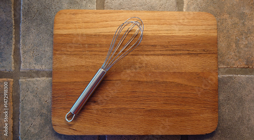 stainless steel French whisk on a wooden cutting board