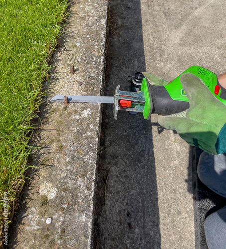 Male hands in green gloves cut metal bolt protruding from a concrete beam with an electric reciprocating saw. photo