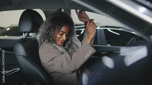 Woman enjoying music while dancing in her car at an indoor parking garage during the day
