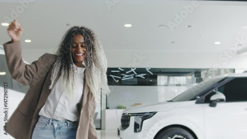 Woman joyfully dances among cars in a modern dealership showcasing a lively atmosphere during daytime