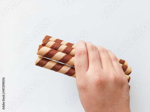 Hand holding striped wafer rolls—crispy, chocolate-filled treats perfect for snack packaging, advertisements, or dessert branding with a clean, appetizing presentation