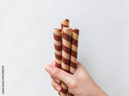 Hand holding striped wafer rolls—crispy, chocolate-filled treats perfect for snack packaging, advertisements, or dessert branding with a clean, appetizing presentation