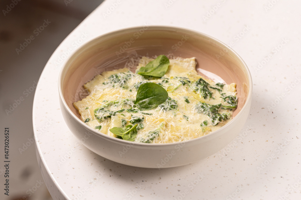 Spinach Ravioli with Creamy Parmesan Sauce.
Fresh ravioli pasta filled with spinach, topped with creamy cheese sauce and garnished with spinach leaves in a modern bowl. Spinach Ravioli with Creamy Parmesan Sauce.
Fresh ravioli pasta filled with spinach, topped with creamy cheese sauce and garnished with spinach leaves in a modern bowl.