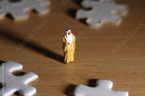 Miniature people toy figure photography. Business alternative concept. A Sultan wearing yellow Bisht (king cloak) standing in the center of four puzzle jigsaw piece. Image photo