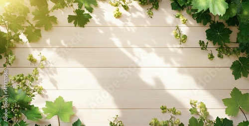 Sunlight illuminates green grapevine leaves arranged on a light wood background, creating a frame.