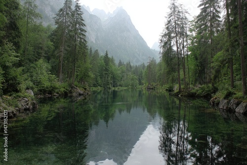 Serene Mountain Lake Reflecting Forest Trees, Tranquil Waters, and Misty Peaks.