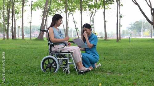 Elderly woman sitting in a wheelchair and being cared for by a female nurse in the park, natural therapy concept Staff or caretakers of the elderly