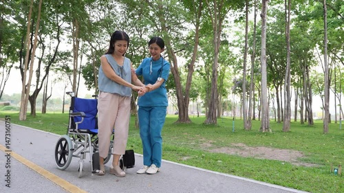 A young Asian doctor takes an elderly woman for a walk in the park. natural therapy concept Employee or caretaker of the elderly