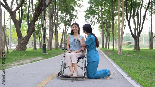 Elderly woman sitting in a wheelchair and being cared for by a female nurse in the park, natural therapy concept Staff or caretakers of the elderly