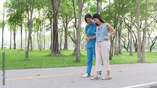 A young Asian doctor takes an elderly woman for a walk in the park. natural therapy concept Employee or caretaker of the elderly