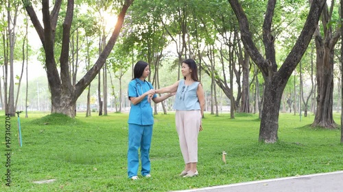 A young Asian doctor takes an elderly woman for a walk in the park. natural therapy concept Employee or caretaker of the elderly
