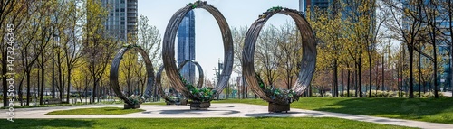 Raising Awareness Through Metal Recycling for a Sustainable Future, Sculptural rings in a park surrounded by trees and urban architecture.