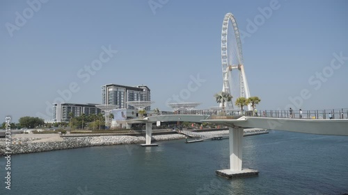 Dubai, United Arab Emirates - February 15 2023: A pedestrian bridge with a massive ferris wheel on the waterfront.