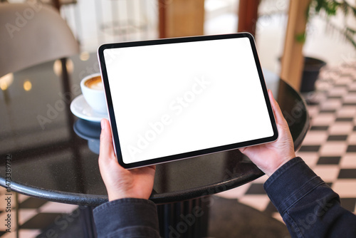 Mockup image of a woman holding digital tablet with blank white desktop screen in cafe