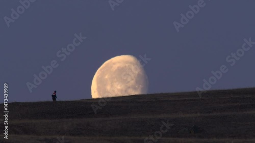 Silhouette of running man on a mountain slope against large moon and night sky 