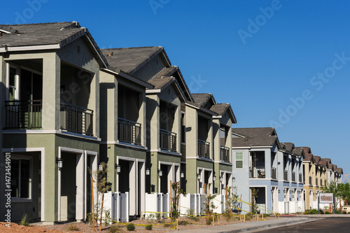A newly developed row of multistory townhomes features balconies, fresh landscaping, and stucco facades, representing residential expansion in a planned housing community.