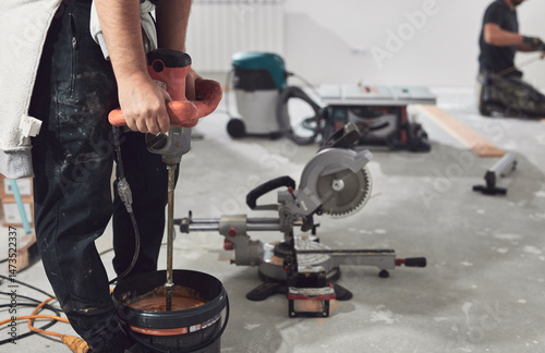 Workers with industrial mixer on a construction site and a bucket of parquet glue.