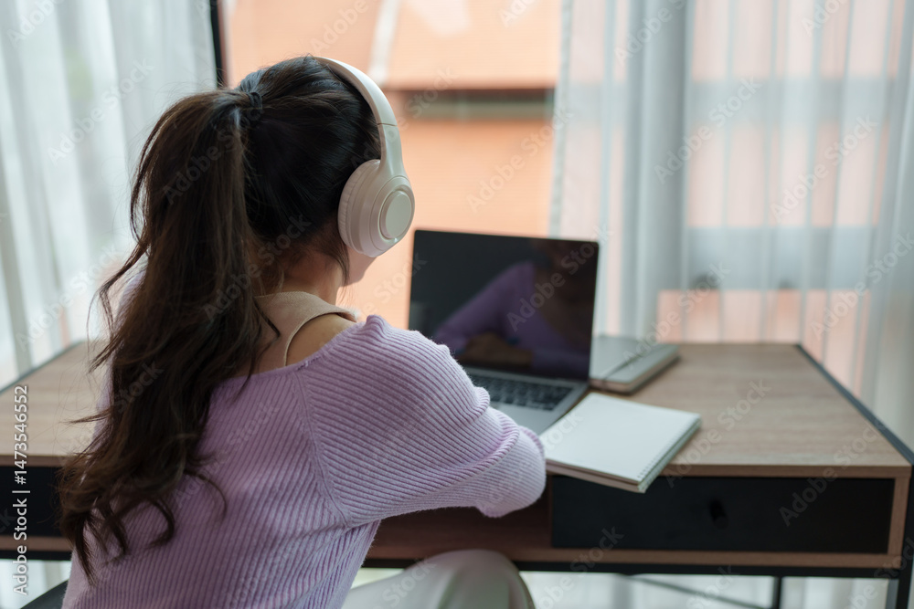 Fototapeta premium Young woman working from home listening music with headphones and laptop