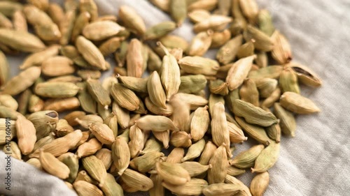 Dried cardamom pods falling on dinner cloth napkin with textured fabric texture. Slow motion. Rotation