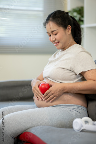 A pregnant Asian woman is making gestures of love to her unborn baby at her home.