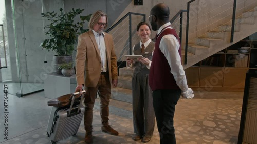 Wallpaper Mural Guest having conversation with hotel receptionist, then handing suitcase to bell boy in modern lobby during check in Torontodigital.ca