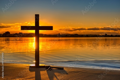 Hammer and three nails by a wooden cross with a wonderful dawn sky over a bay of water. photo
