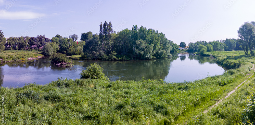Landscape with grass field, river and blue sky