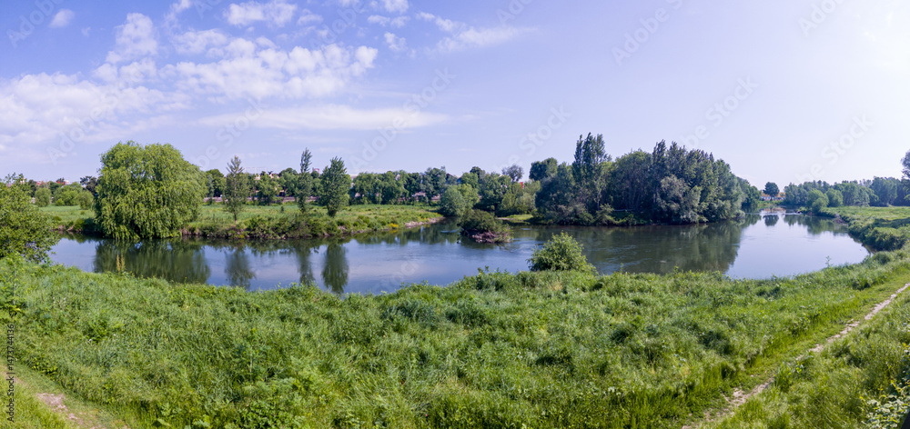 Landscape with grass field, river and blue sky