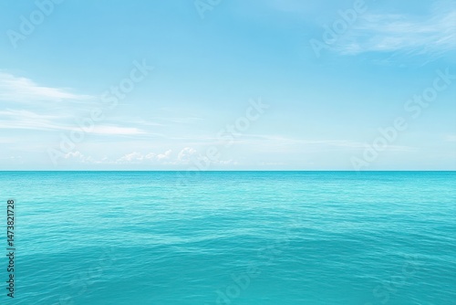 Tranquil expanse of turquoise water meeting a light blue sky dotted with fluffy white clouds