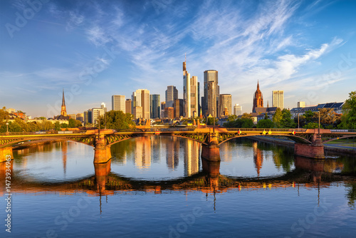 Fototapeta Naklejka Na Ścianę i Meble -  Sunrise view of the modern skyline of Frankfurt, Germany, with golden sunlight shining on the office skyscrapers of the city