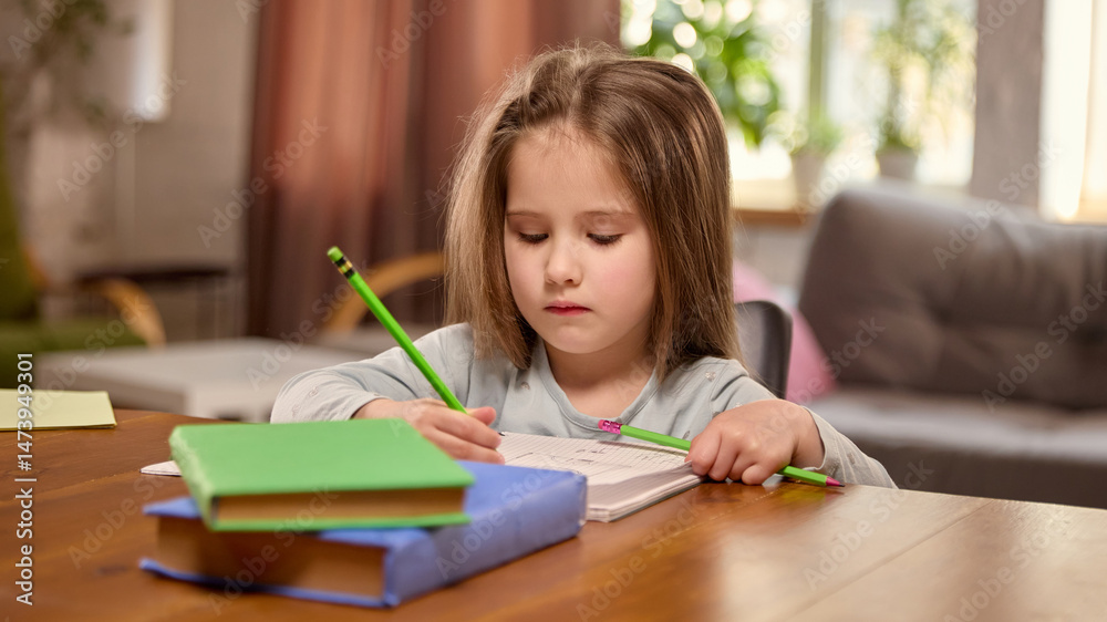 Child girl sitting at table, writing in notebook with pencils in living room at home. Beginning of learning, preschool development, academic skills. Concept of home learning, schoolwork, childhood Child girl sitting at table, writing in notebook with pencils in living room at home. Beginning of learning, preschool development, academic skills. Concept of home learning, schoolwork, childhood