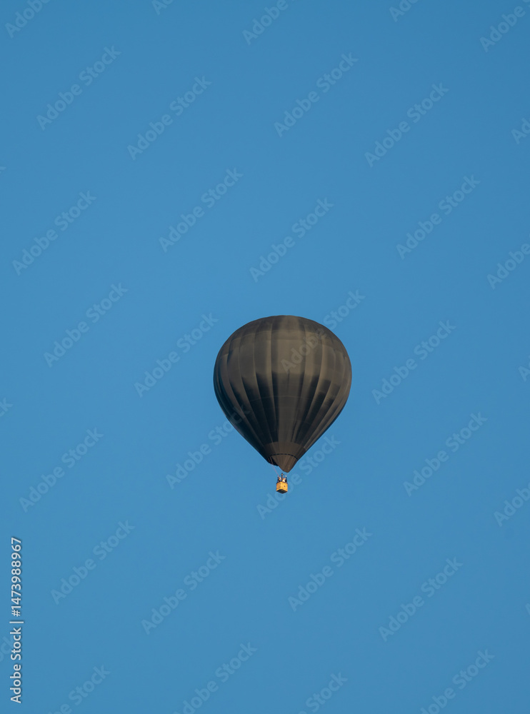 Fototapeta premium A black hot air balloon is floating in the sky above a blue sky