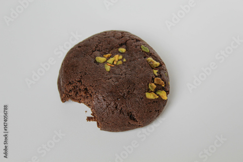 A bitten chocolate soft cookie, with green pistachio topping, isolated on white background