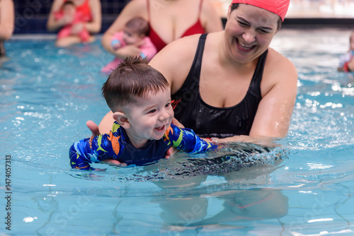 Smiling baby boy learning to swim with instructor in indoor pool