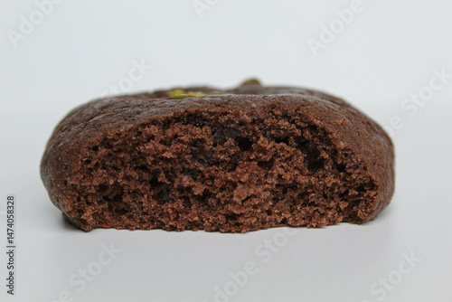 A bitten chocolate soft cookie, with green pistachio topping, isolated on white background