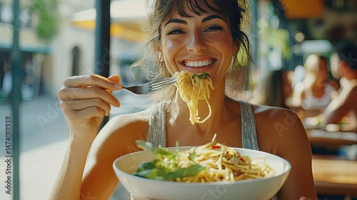 A smiling woman with long, wavy hair holds a wooden bowl filled with salad, while a spoon is poised near her mouth.