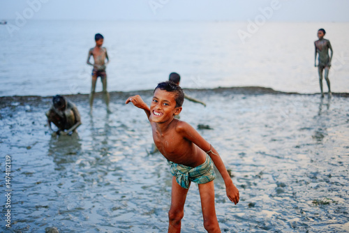 Fotografie Village kids playing near a riverside muddy beach