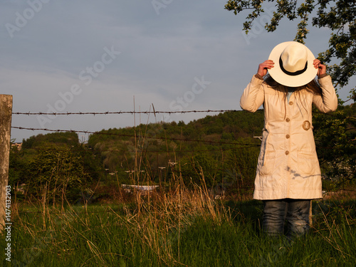 Woman putting on straw boater hat in farm field countryside