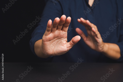 Quadro em tela Close-up of man raising hands in defensive gesture on black background, concept of refusal or stop
