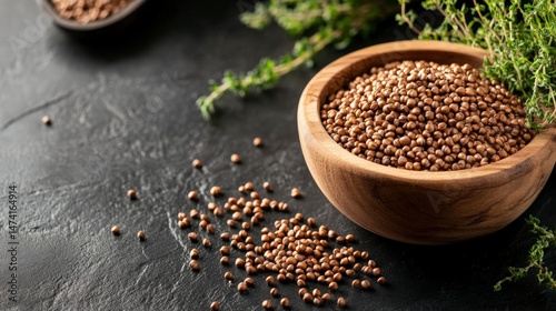 A wooden bowl filled with chia seeds on a dark surface, with a sprig of chia plant in the background.