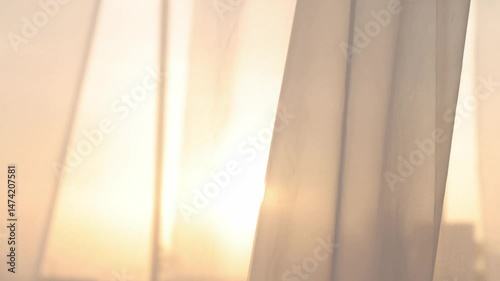 Light breezy sheer curtain blowing in the wind with sunset behind it